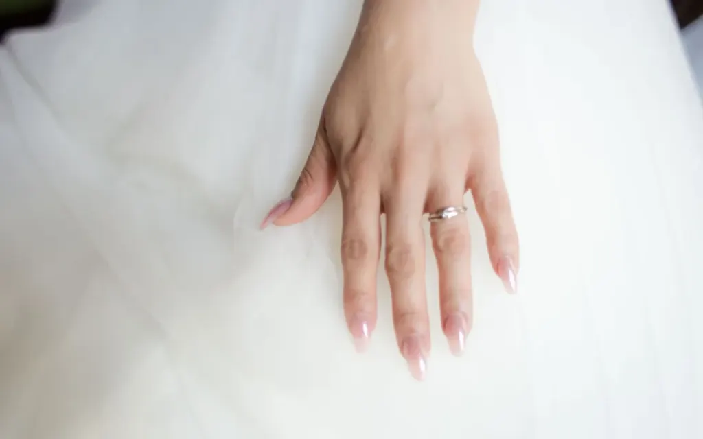 Dłoń panny młodej z migdałowym manicure w odcieniu nude na tiulowej sukni